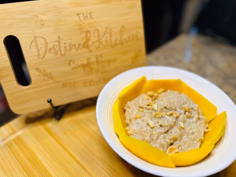 A beautifully plated serving of Thai mango sticky rice, featuring a mound of sticky rice drizzled with creamy coconut sauce, alongside ripe mango slices. The dish is garnished with toasted sesame seeds and served on a rustic wooden plate for an authentic presentation.