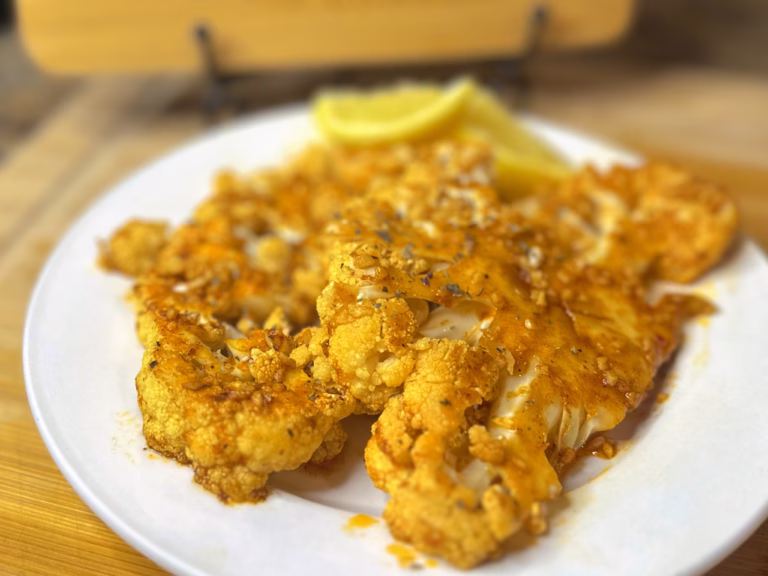 Golden zesty baked lemon garlic cauliflower steaks on a white plate, seasoned with lemon-garlic basil marinade and served with lemon wedges