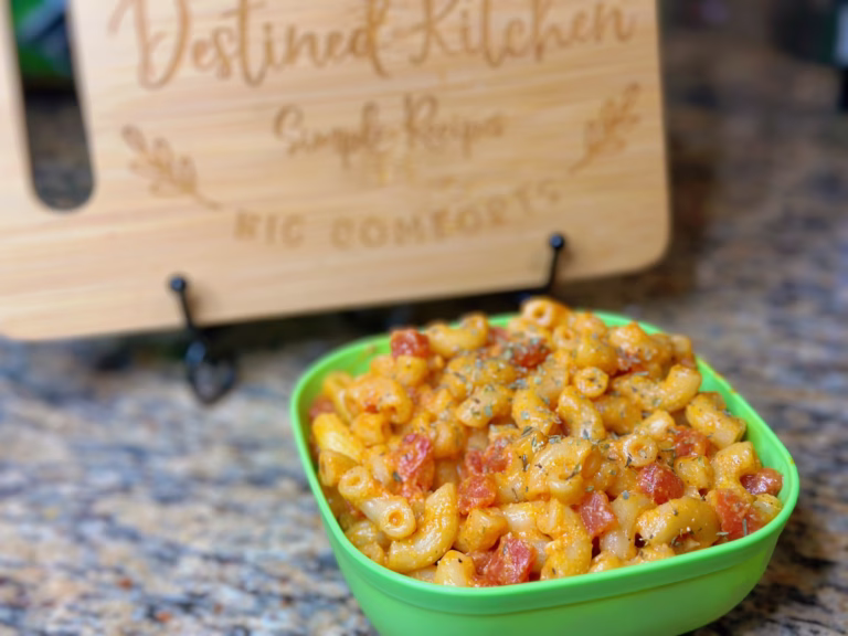 Bowl of elbow macaroni recipe with tomatoes in a green dish, served in front of a Destined Kitchen sign – a comforting vegan pasta meal